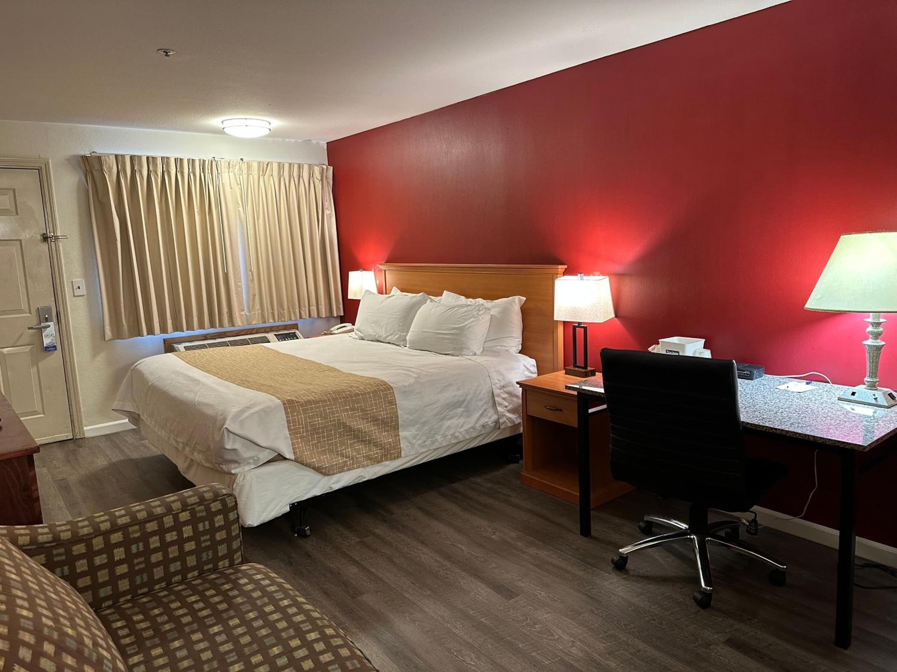 Une chambre d’hôtel équipée d’un lit, d’un bureau, d’une chaise, d’une lampe de bureau, d’un téléphone et d’une fenêtre avec des rideaux.
