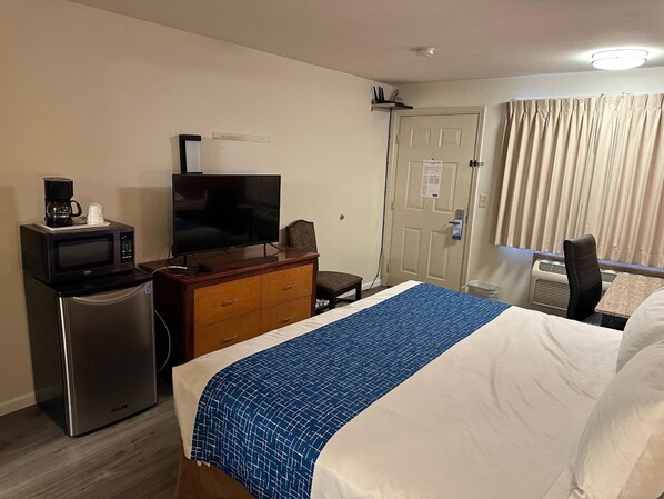 Habitación de hotel con cama, televisión, microondas, refrigerador, escritorio y una silla.