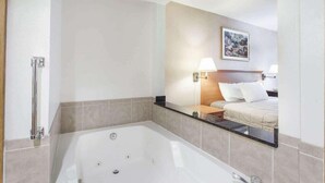 Ein modernes Badezimmer mit einer großen Badewanne, einer Duschkabine und einem Bett mit Nachtisch.
