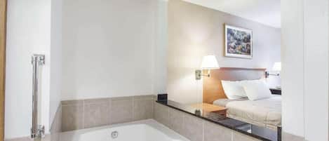 A modern bathroom with a large bathtub, a shower area, and a bed with a nightstand.