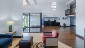 Een ruime lobby met een receptiebalie, een blauwe bank, een rode fauteuil en een moderne hanglamp.