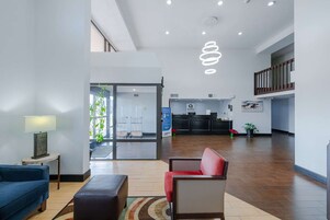 A spacious lobby with a reception desk, a blue sofa, a red chair, and a modern pendant light.