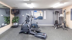 Un gimnasio con equipo de ejercicio, un televisor y un cuadro de una montaña.