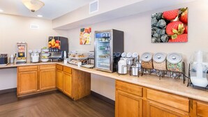 Una barra de desayuno con máquinas de café, un refrigerador y varios recipientes de comida.