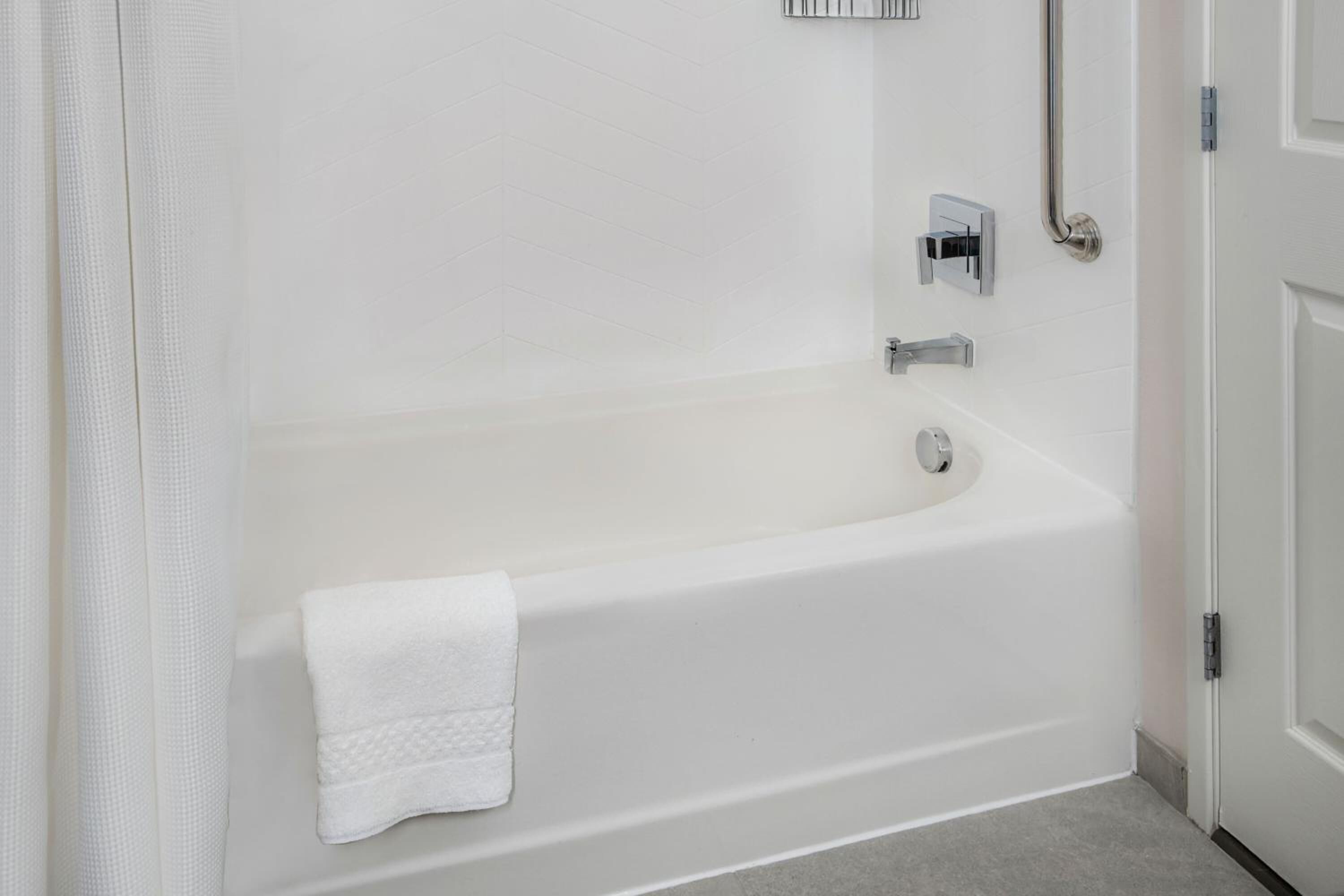 A white bathtub with a towel, a shower control panel, and a door.