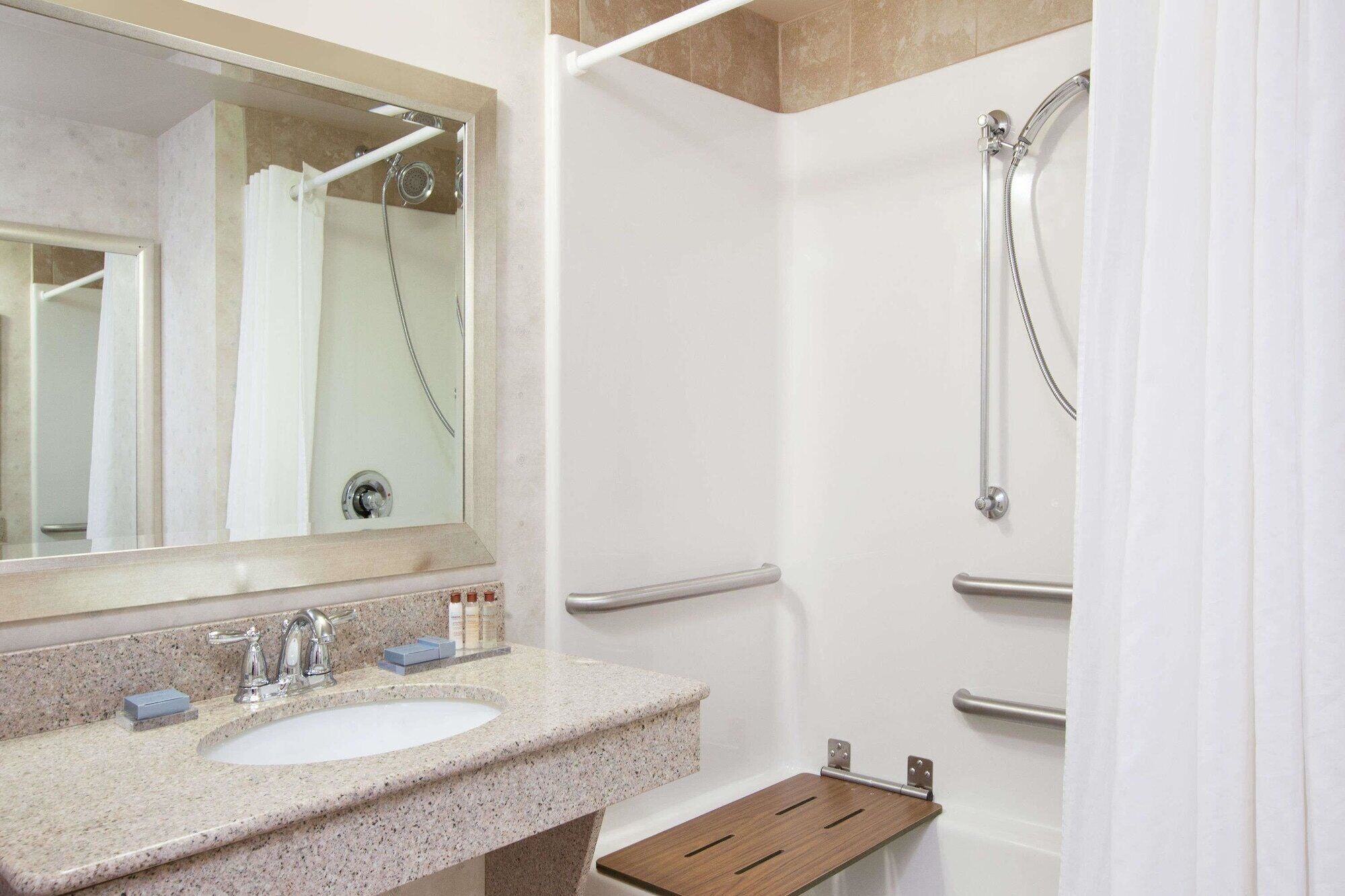 A modern bathroom with a granite countertop sink, a mirror, a shower with a handheld showerhead, and a towel rack.