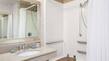 A modern bathroom with a granite countertop sink, a mirror, a shower with a handheld showerhead, and a towel rack.