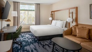A hotel room with a bed, a sofa, a desk with a chair, a TV, and a window with curtains. - Fairfield by Marriott Inn & Suites Rome NY (Rome)