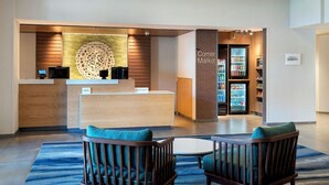 A reception area with a wooden reception desk, a coffee machine, and a Corner Market sign. There are two wooden chairs with teal cushions in front of the desk. - Fairfield by Marriott Inn & Suites Rome NY (Rome)