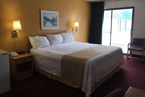 Quarto de hotel com uma cama grande, duas luminárias de cabeceira, um quadro na parede e vista pela janela.