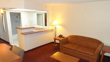 A compact hotel room with a kitchenette, a sofa, a small table, and a lamp.