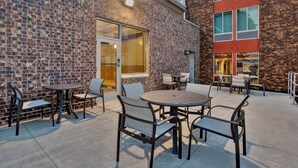 An outdoor patio with brick walls, metal furniture, and a glass door leading to an interior space. - Holiday Inn Express And Suite Eden Prairie Minneapolis (Eden Prairie)