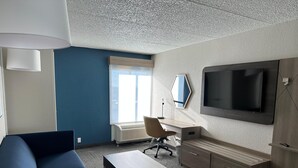 A modern hotel room with a sofa, a desk, a chair, a TV, and a large window. - Holiday Inn Express And Suite Eden Prairie Minneapolis (Eden Prairie)