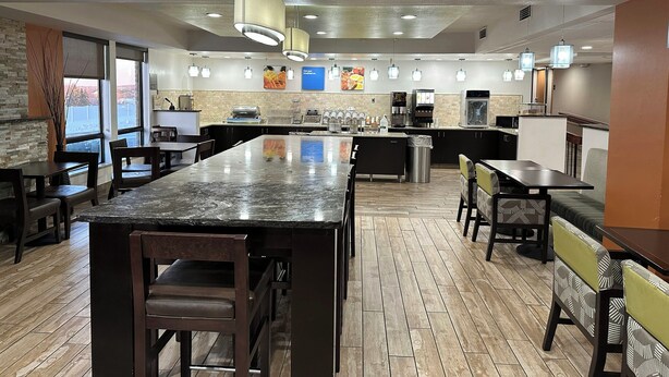 A restaurant with a central island, seating arrangements, and a kitchen area. - Holiday Inn Express And Suite Eden Prairie Minneapolis (Eden Prairie)