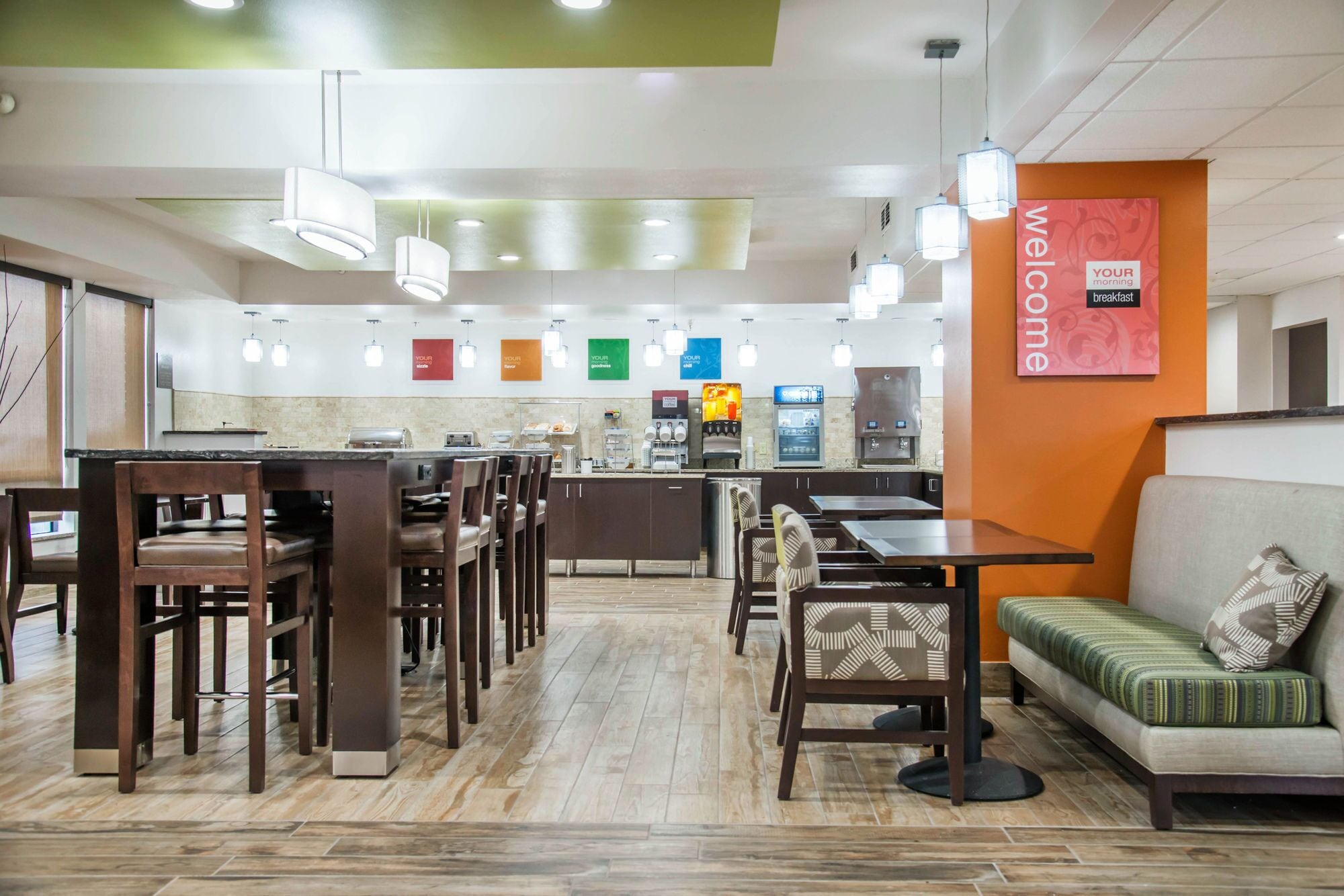 Un moderno comedor con una barra central, diversas opciones de asiento y un cartel que dice 'Welcome'.