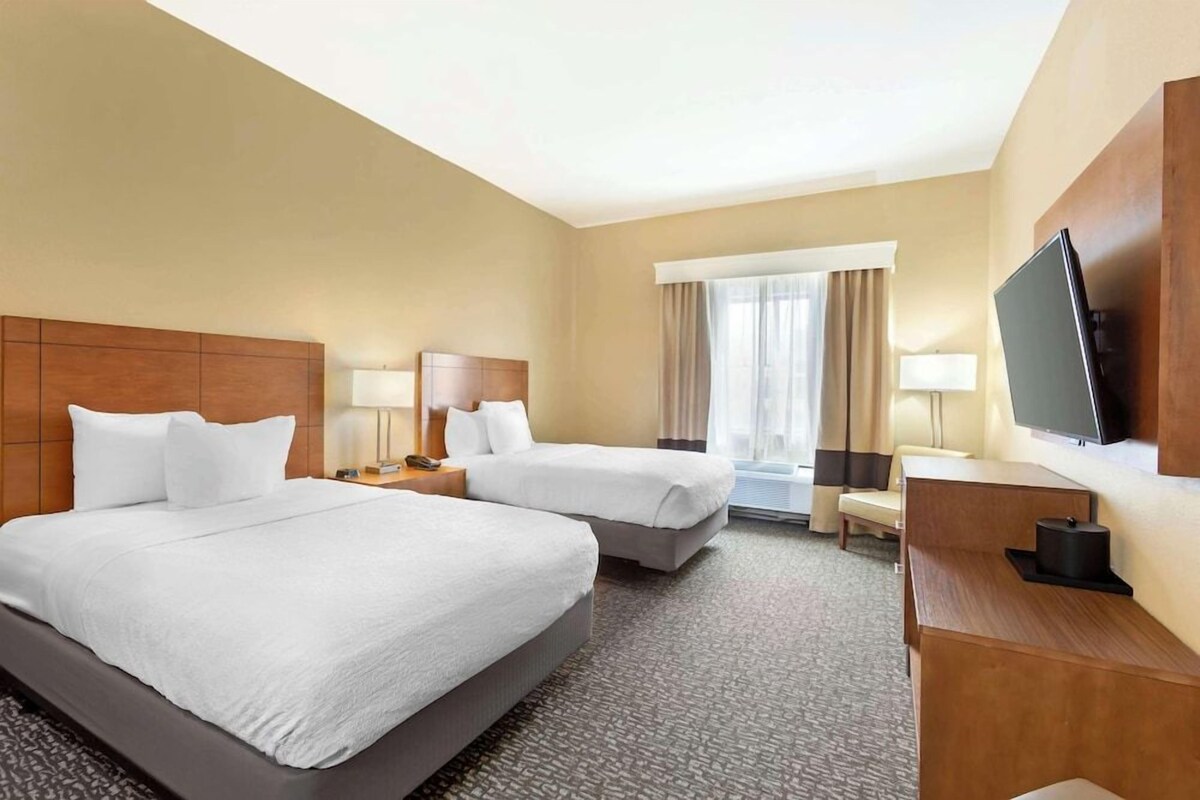 A hotel room with two beds, a television, a desk, and a window with curtains.