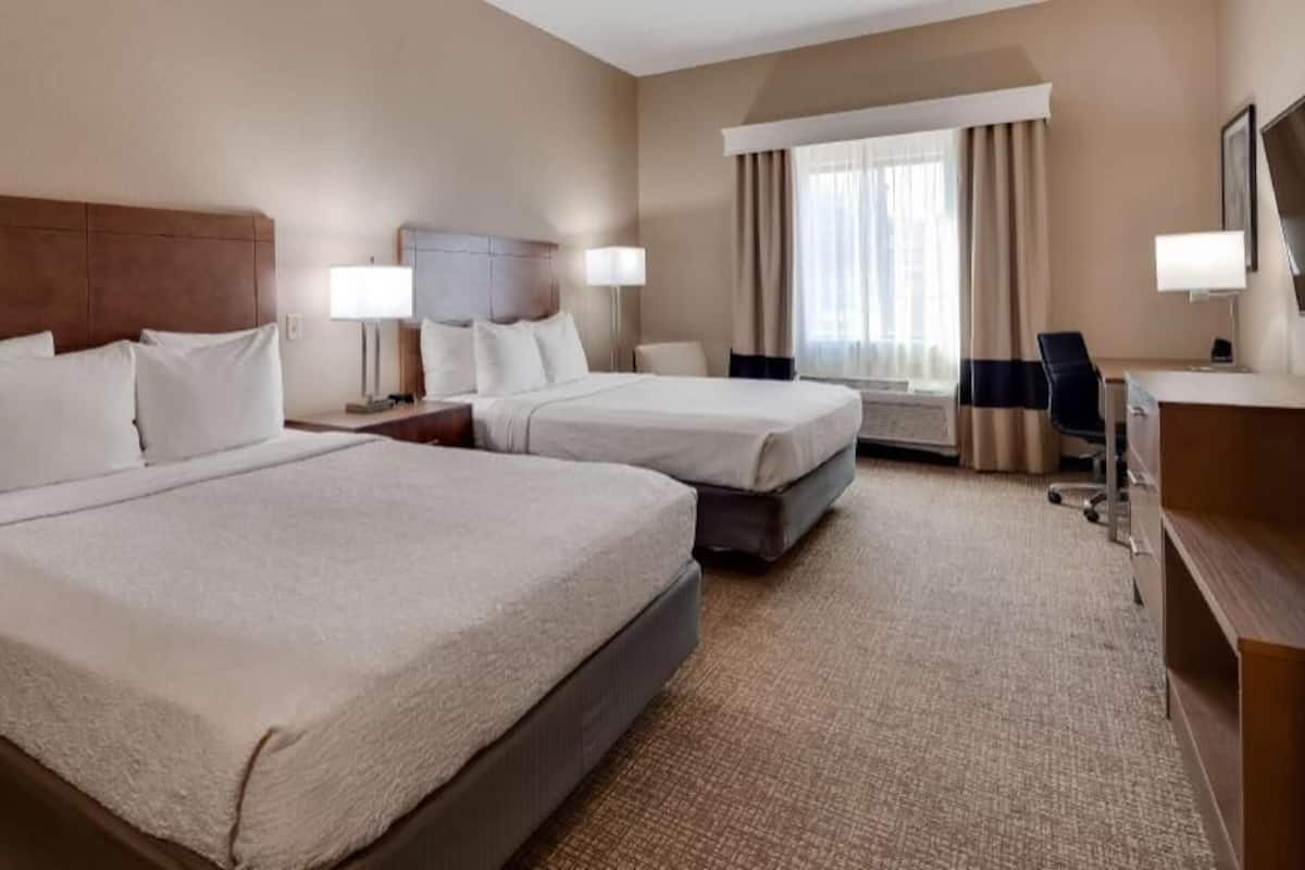 A hotel room with two beds, a desk, a chair, a TV, and a window with curtains.