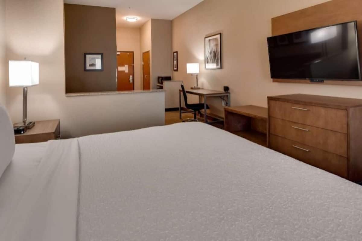 A hotel room with a bed, a desk, a chair, a TV, a dresser, and a mirror.