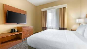 A hotel room with a large bed, a flat-screen TV mounted on the wall, a wooden desk, and a window with curtains.