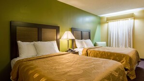 Habitación de hotel con dos camas, una mesita de noche con lámpara y una ventana con cortinas.