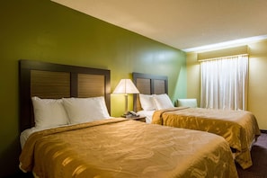 A hotel room with two beds, a nightstand with a lamp, and a window with curtains. - Red Roof Inn Jasper (Jasper)