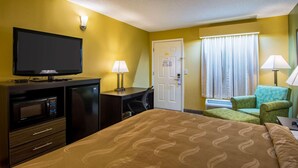 Habitación de hotel con cama, escritorio con computadora, televisor, microondas, silla y puerta.