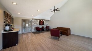A spacious living area with a high ceiling, a ceiling fan, and a stone accent wall. There are two red chairs and a brown sofa. - Red Roof Inn Jasper (Jasper)