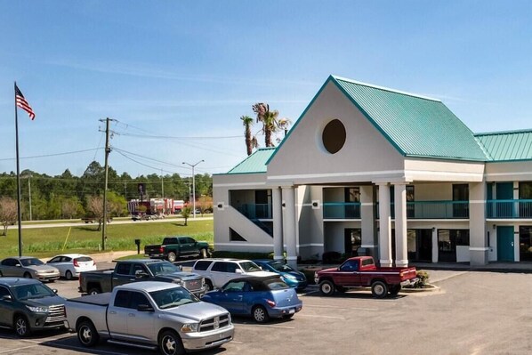 A hotel with a green roof, white exterior, and a parking lot with several cars. - Econo Lodge Moss Point - Pascagoula (Moss Point)
