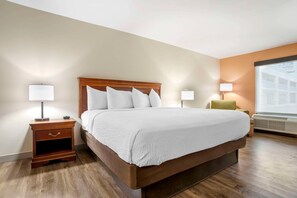 A hotel room with a large bed, bedside lamps, a nightstand, a chair, and a window with a view. - Econo Lodge Moss Point - Pascagoula (Moss Point)