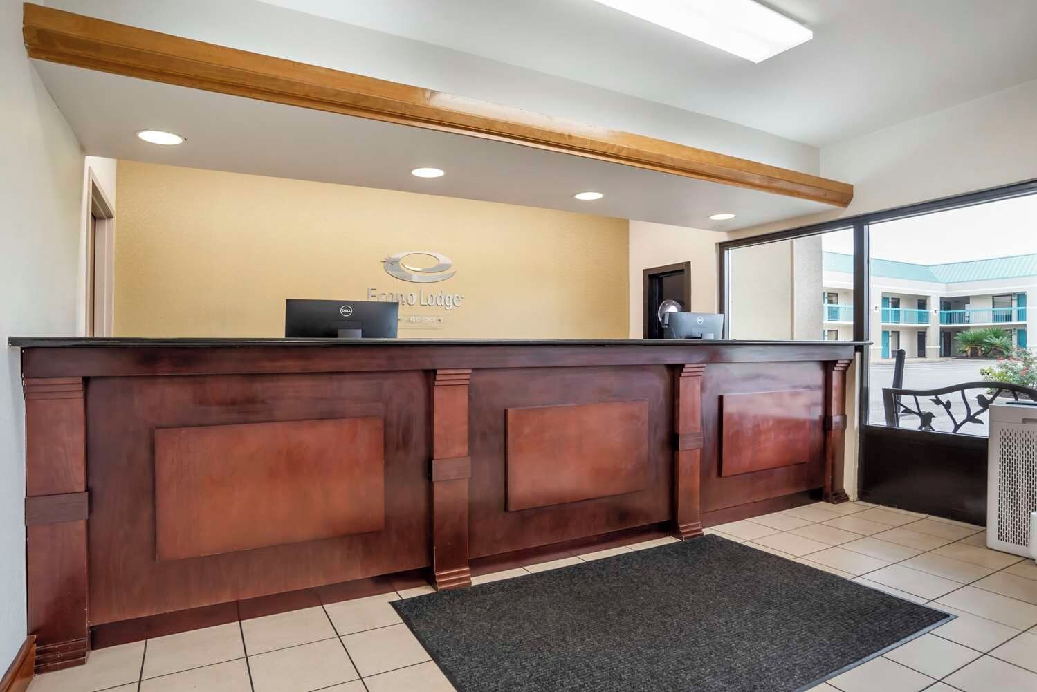 A reception desk with a wooden finish, a sign above it, and a view of the building outside.