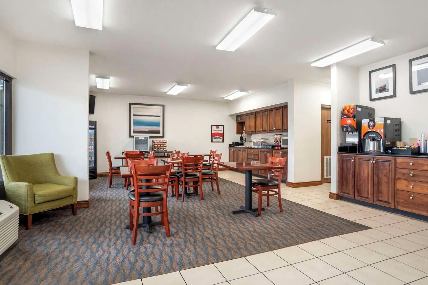 A hotel room with a dining area, kitchenette, and a green armchair.