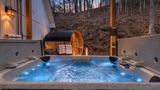 A hot tub with a wooden barrel and a stone wall, surrounded by a forested area. - 1 mile Pkwy~Single level ~ Sauna, Outdoor Movies (Pigeon Forge)