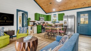 A spacious living room with a wooden ceiling, a dining area with green cabinets, and a kitchen with a stainless steel refrigerator. - 1 mile Pkwy~Single level ~ Sauna, Outdoor Movies (Pigeon Forge)