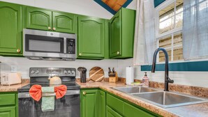 A kitchen with green cabinets, a stainless steel stove, a microwave, a sink, and a window with a view of the outdoors. - 1 mile Pkwy~Single level ~ Sauna, Outdoor Movies (Pigeon Forge)