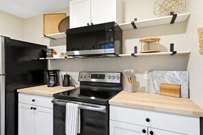 A modern kitchen with a black refrigerator, stainless steel appliances, white cabinetry, and wooden countertops.
