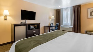 Et hotelværelse med seng, skrivebord, fjernsyn, lampe, stol og et vindue med gardiner.