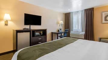 Habitación de hotel con cama, escritorio, televisor, lámpara, silla y ventana con cortinas.