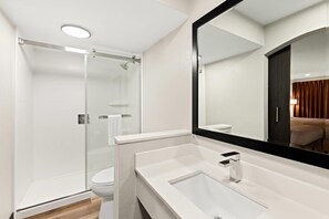 A modern bathroom with a glass-enclosed shower, a white sink with a black faucet, and a large mirror. - Quality Inn & Suites Dumas, AR (Dumas)