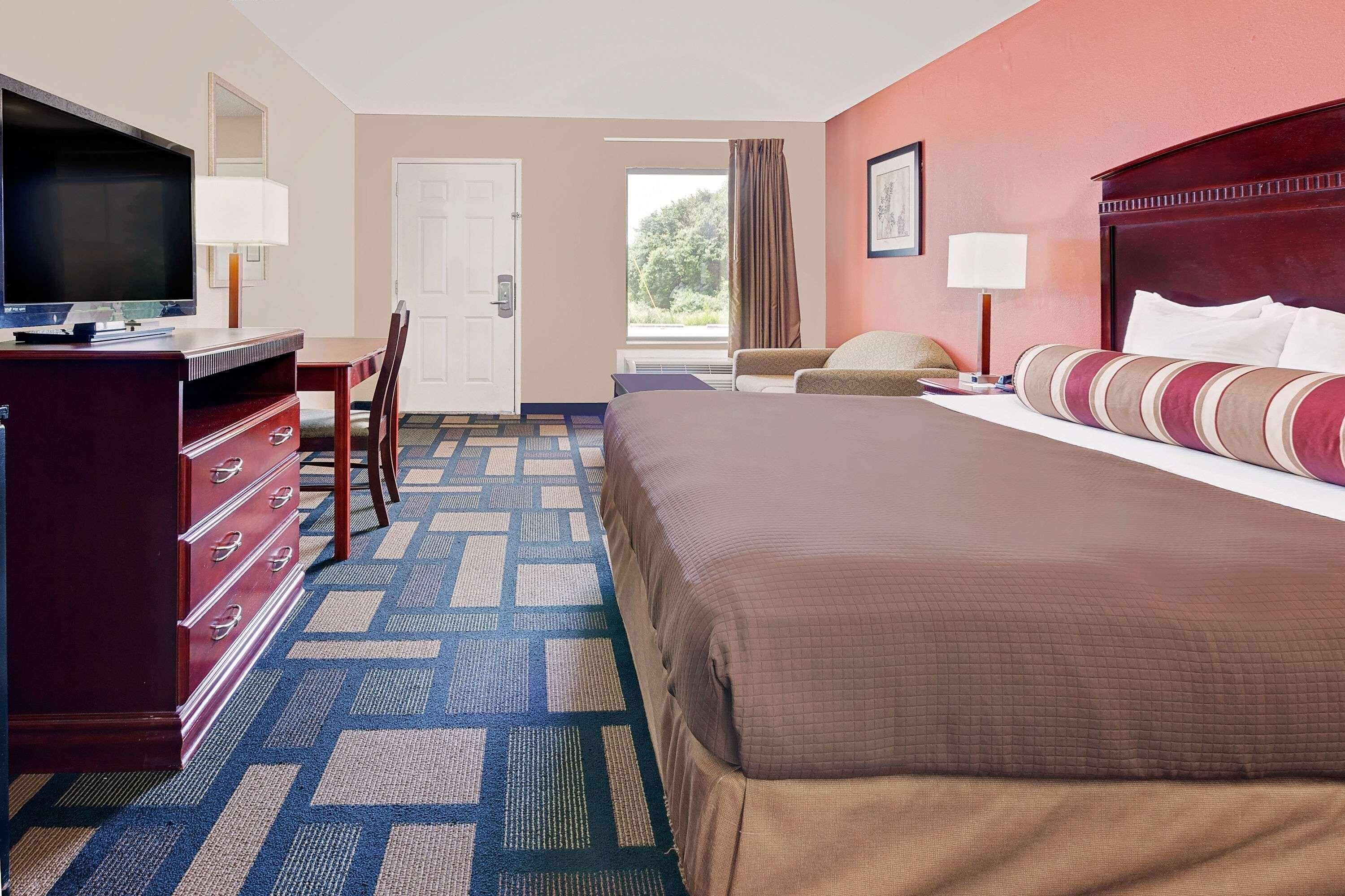 Une chambre d’hôtel avec un lit, un bureau avec une télévision, une commode et une fenêtre avec des rideaux.