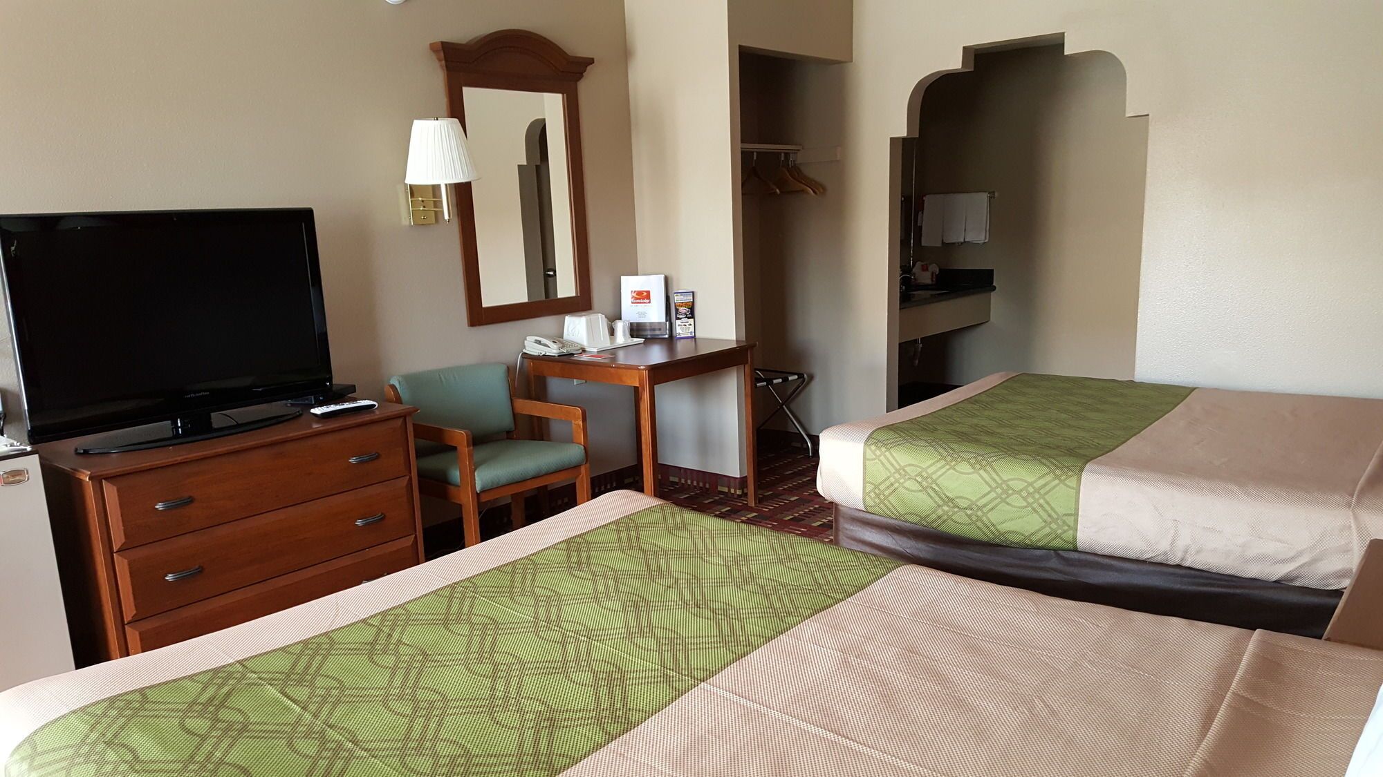 A hotel room with two beds, a desk with a chair, a television, and a mirror.