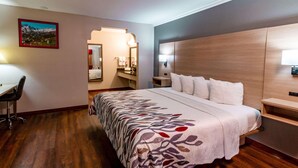 Ein Hotelzimmer mit einem großen Bett, einem Schreibtisch und einem durch einen Bogen sichtbaren Badezimmer.