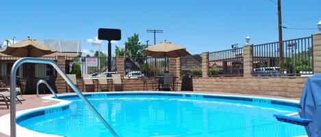 A swimming pool with a metal ladder, lounge chairs, and umbrellas.