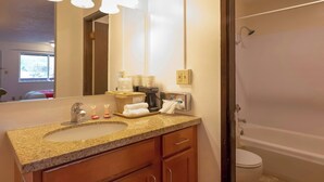Une salle de bain avec un comptoir en granit, un lavabo, un miroir, un porte-serviettes, une douche et des toilettes.