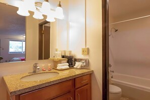 Un baño con encimera de granito, lavamanos, espejo, toallero, ducha e inodoro.