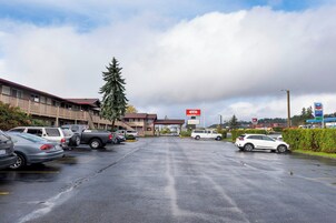 A hotel with a red sign, a parking lot with cars, and a gas station in the background.