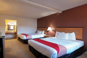 A hotel room with two beds, a nightstand, a lamp, a mirror, and a small table with toiletries.