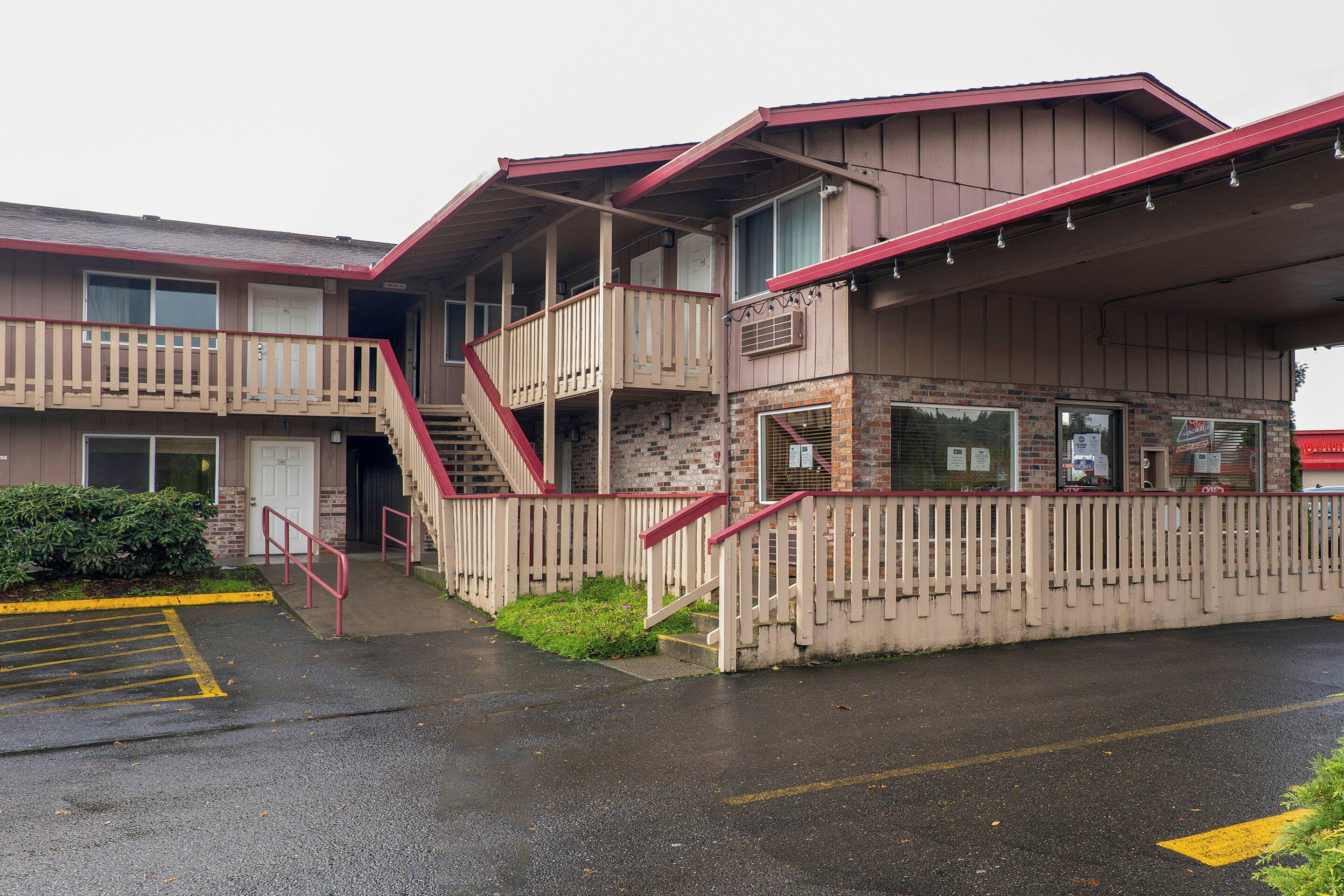 Un motel de dos pisos con una paleta de colores rojo y beige, un área exterior cubierta y un estacionamiento.