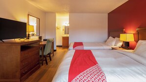 Une chambre d’hôtel avec deux lits, un bureau, une télévision et une salle de bain visible à travers une porte ouverte.