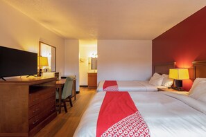 Habitación de hotel con dos camas, un escritorio, televisor y baño visible a través de una puerta abierta.