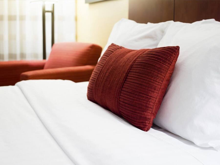 Una cama bien hecha con sábanas blancas y una única almohada roja.